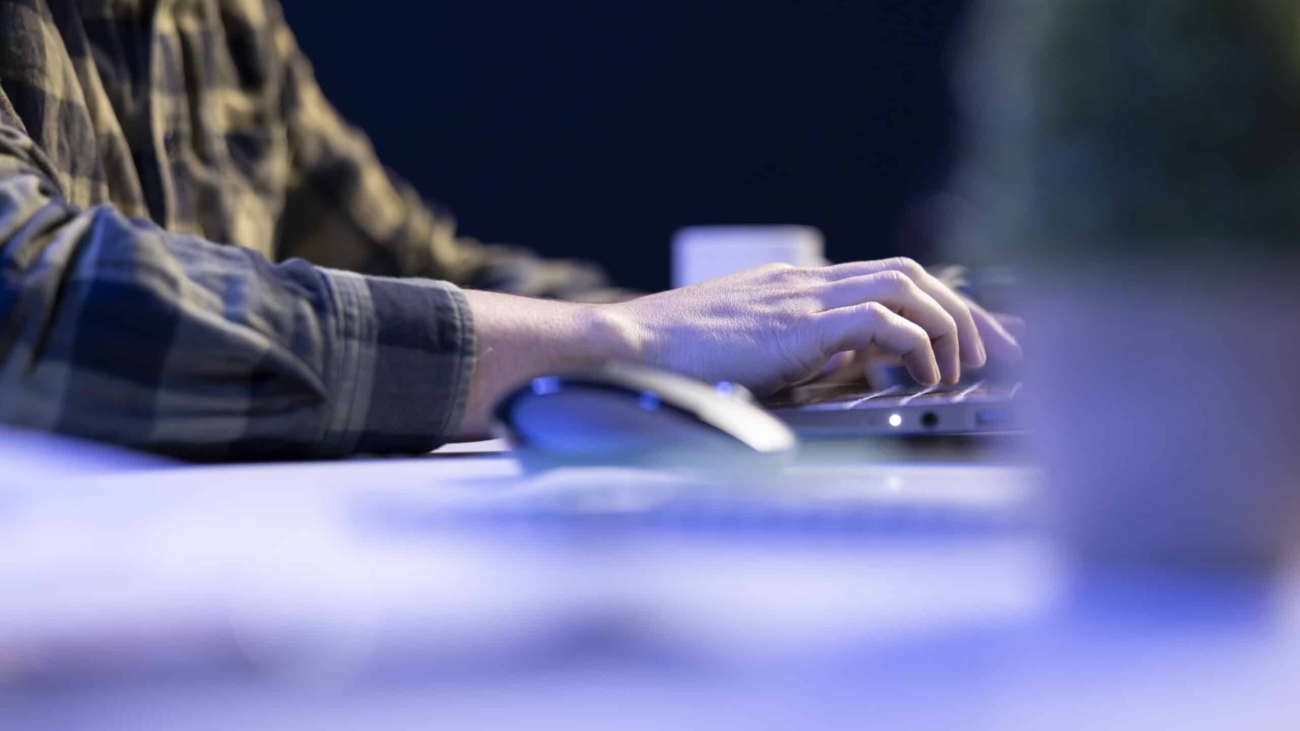 Closeup shot of male individual using laptop keyboard and mouse at office desk to surf the internet. Person typing on digital device, finishing tedious paperwork.