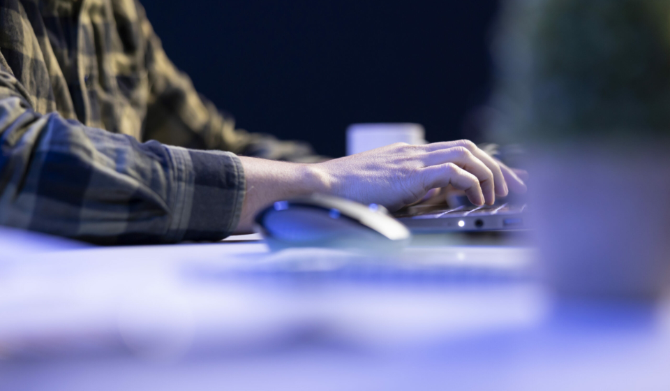 Closeup shot of male individual using laptop keyboard and mouse at office desk to surf the internet. Person typing on digital device, finishing tedious paperwork.